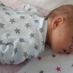 Słodki noworodek śpi z otwartą buzią, ubrany w pajacyk w gwiazdki.