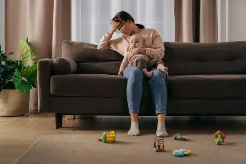 Zmęczona samotna matka z dzieckiem na kolanach, otoczona zabawkami.