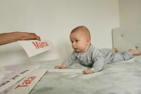 Zaciekawione niemowlę na brzuchu patrzy na kartki z napisami "Mama" i "Tata".