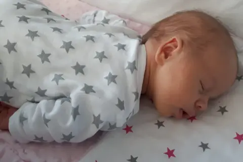 Słodki noworodek śpi z otwartą buzią, ubrany w pajacyk w gwiazdki.