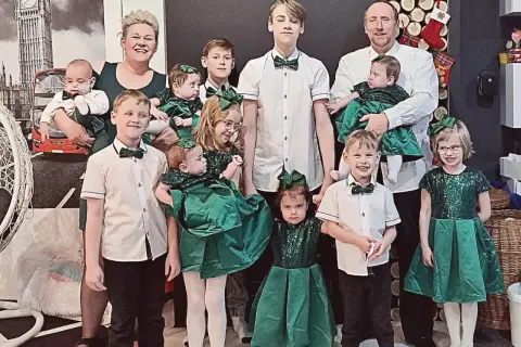 Rodzina z pięcioraczkami w zielonych strojach, pozująca do zdjęcia.