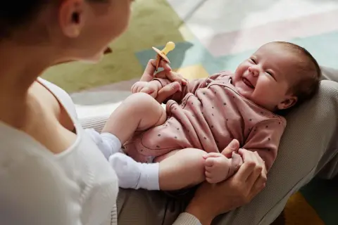 Mama bawi się z dzieckiem, które radośnie gaworzy, trzymając smoczek.