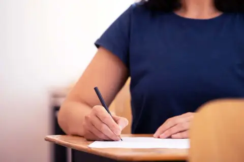 Uczeń pisze wypracowanie, które może być jedną z lektur z gwiazdką. Skupienie na kartce papieru i ołówku.