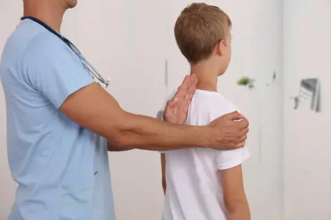Lekarz bada chłopca, sprawdzając jego postawę. Może to być część diagnostyki zespołu Marfana, gdzie obserwuje się różne objawy.