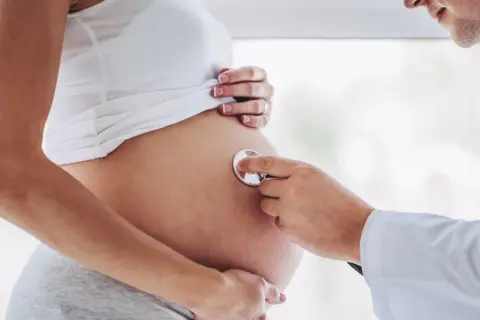Lekarz osłuchuje brzuch ciężarnej kobiety, która jest w 24 tygodniu ciąży. Słychać bicie serca dziecka.