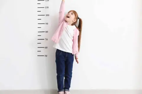 Dziewczynka z kucykami mierzy swój wzrost przy podziałce. Czyżby czekał ją gigantyzm?