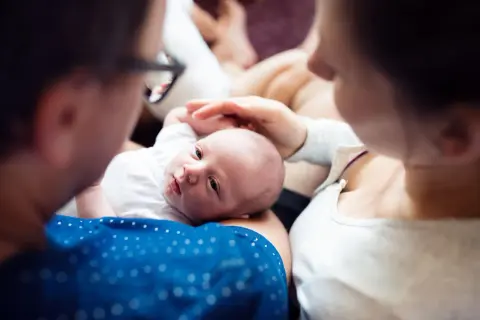 Rodzice czule otaczają noworodka. To piękny obraz opieki na żone po porodzie, pełen miłości i bliskości.