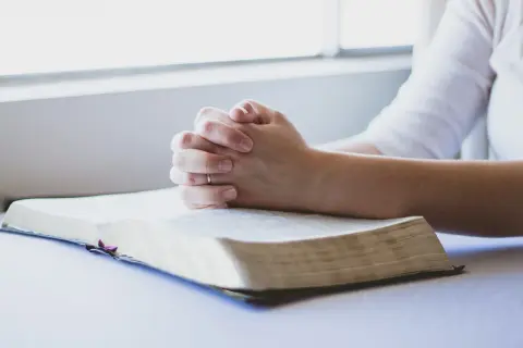 Dłonie złożone w modlitwie nad otwartą Biblią. To chwila głębokiej modlitwy za dzieci, o ich zdrowie i szczęście.