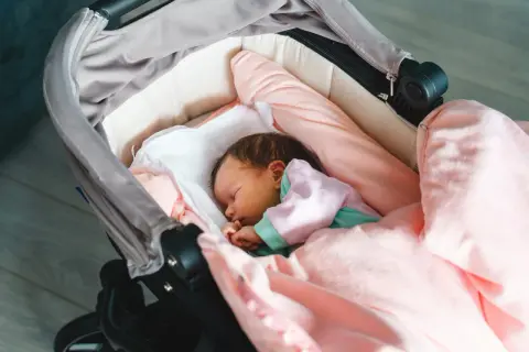 Słodki noworodek śpi w wózku, otulony różowymi kocykami. To idealny moment na pierwszy spacer z noworodkiem.