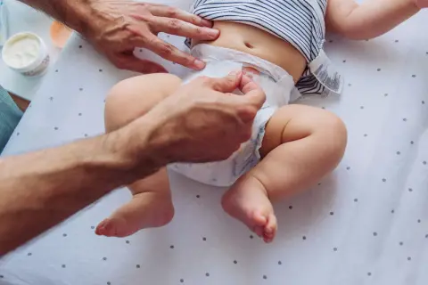 Rączki taty zmieniają pieluszkę, na której widać śluz w kupie niemowlaka.