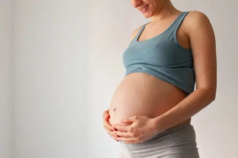 Brzuch kobiety w ciąży, trzymany w dłoniach. Zdjęcie pokazuje, jak wygląda czop śluzowy, choć nie jest on widoczny bezpośrednio.