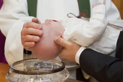 Chrzest dziecka. Woda święcona spływa na główkę niemowlęcia. Warto pomyśleć, ile daje się na chrzciny.