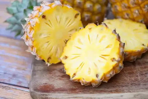 Dwa przekrojone ananasy na desce, jeden z nich wygląda jak ananas w ciąży, z widocznym wnętrzem i koroną.
