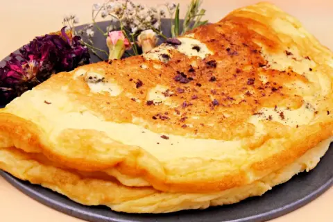 Puszysty omlet dla niemowlaka, delikatnie przyrumieniony, z ozdobnymi suszonymi kwiatami na talerzu.