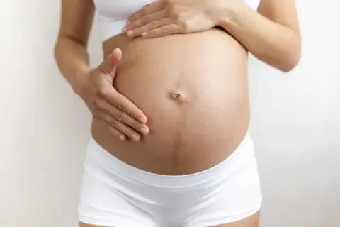 Brzuch kobiety w ciąży z widoczną linea negra, delikatnie dotykany dłońmi.