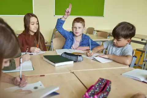 Chłopiec z podniesioną ręką, gotów odpowiedzieć na pytanie: "Od ilu procent jest 3?". Dzieci piszą w zeszytach.