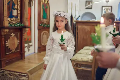 Dziewczynka w białej sukni i wianku trzyma świecę. To ważny dzień, w której klasie komunia?