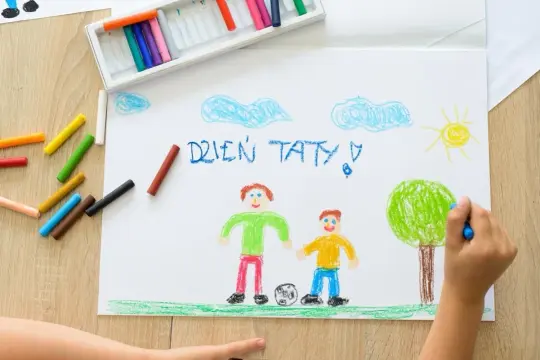 Dziecko rysuje kredkami życzenia na Dzień Taty: uśmiechniętego tatę z synem i piłkę.