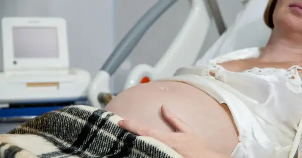 Kobieta w szpitalnym łóżku, z ręką na brzuchu, czeka na poród. Obok monitor KTG, który pomaga ocenić stan dziecka i może sugerować, jak przyspieszyć poród.