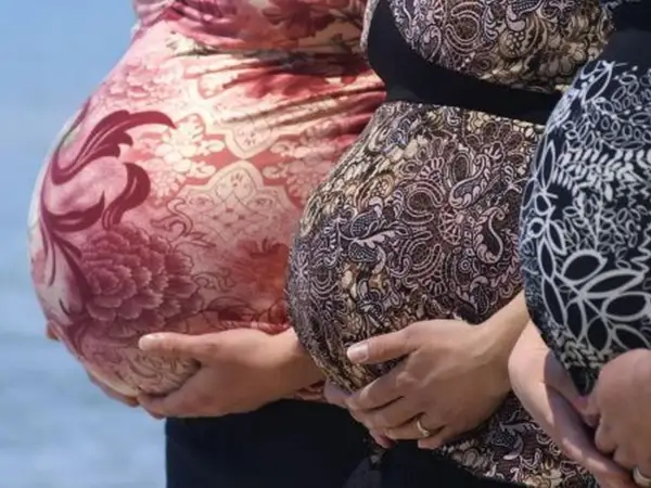 Trzy brzuchy ciążowe w różnych wzorach sukienek, symbolizujące trymestry ciąży.