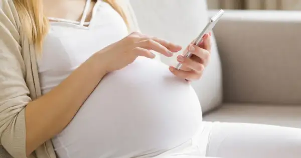 Kobieta w 24. tygodniu ciąży przegląda coś na telefonie, siedząc na kanapie.