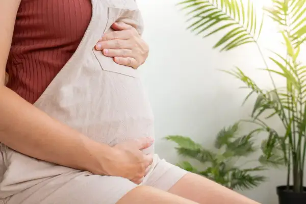 Czekając na poród, gdy szyjka macicy ma 2 cm, kobieta w ciąży trzyma się za brzuch.