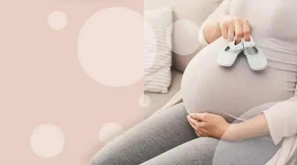 Brzuch ciężarnej kobiety z maleńkimi bucikami. Czas oczekiwania na poród.