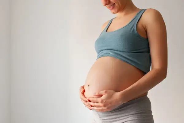 Brzuch kobiety w ciąży, trzymany w dłoniach. Zdjęcie pokazuje, jak wygląda czop śluzowy, choć nie jest on widoczny bezpośrednio.