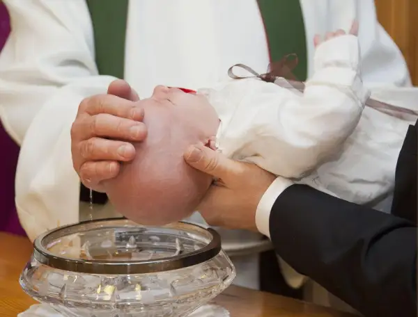 Chrzest dziecka. Woda święcona spływa na główkę niemowlęcia. Warto pomyśleć, ile daje się na chrzciny.