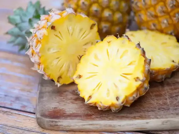 Dwa przekrojone ananasy na desce, jeden z nich wygląda jak ananas w ciąży, z widocznym wnętrzem i koroną.