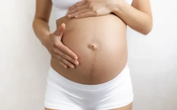 Brzuch kobiety w ciąży z widoczną linea negra, delikatnie dotykany dłońmi.