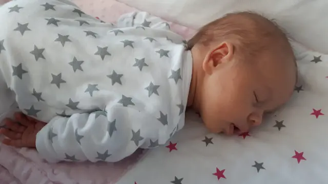Słodki noworodek śpi z otwartą buzią, ubrany w pajacyk w gwiazdki.